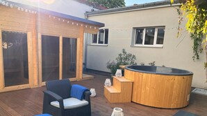Un espacio al aire libre cubierto con mobiliario de madera, un jacuzzi y plantas en macetas.