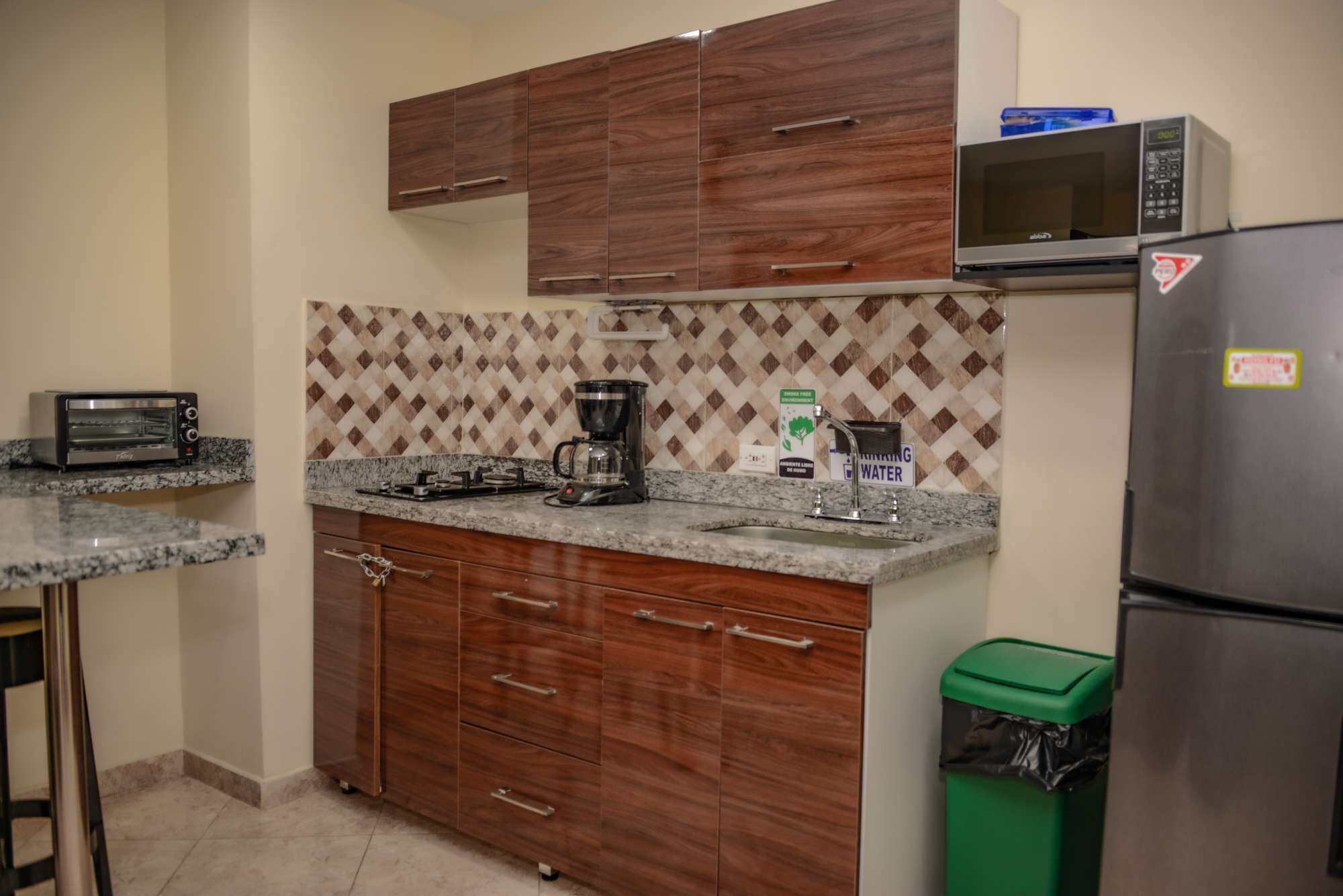 A kitchen with wooden cabinets, a microwave, a toaster, a coffee maker, and a trash bin.