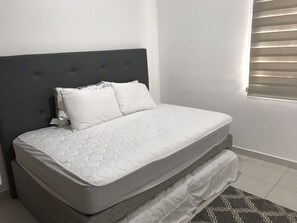 Cozy retreat with a single bed, quilted mattress, and two pillows, set against a wall with a window and horizontal blinds.