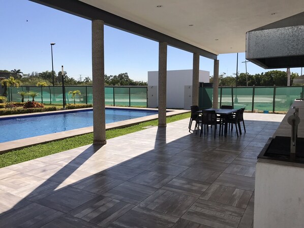 Relax by the pool under a shaded patio with a dining table and chairs.
