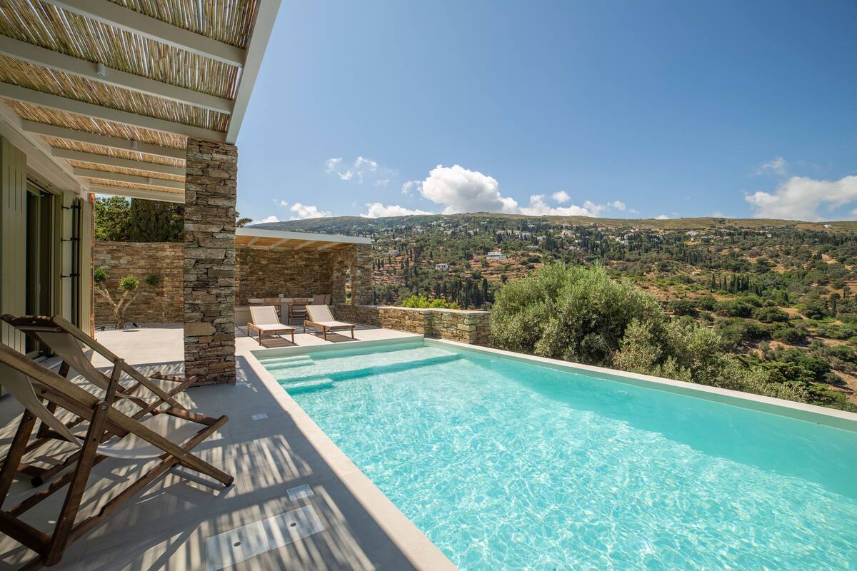 A pool with clear blue water, surrounded by stone walls and wooden lounge chairs.