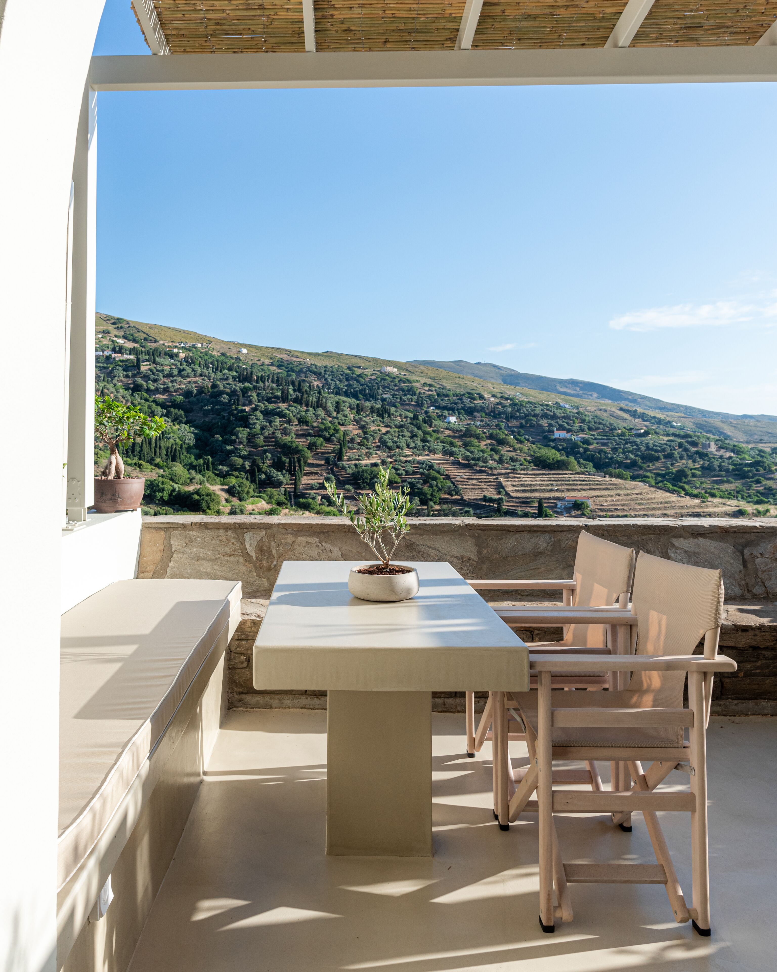 Een terras buiten met een tafel, stoelen, een bloempot en uitzicht op een glooiend landschap.