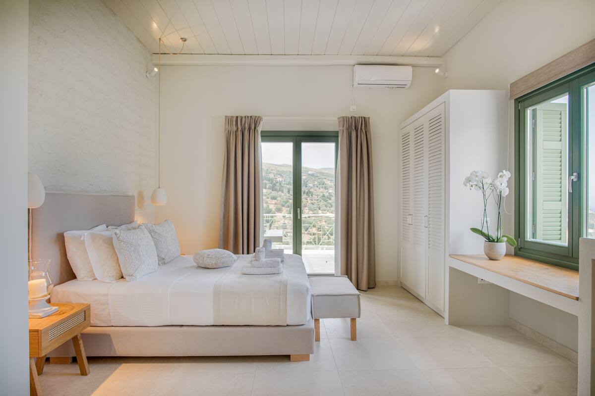 A bedroom with a bed, bedside table, lamp, curtains, and a window with a view.