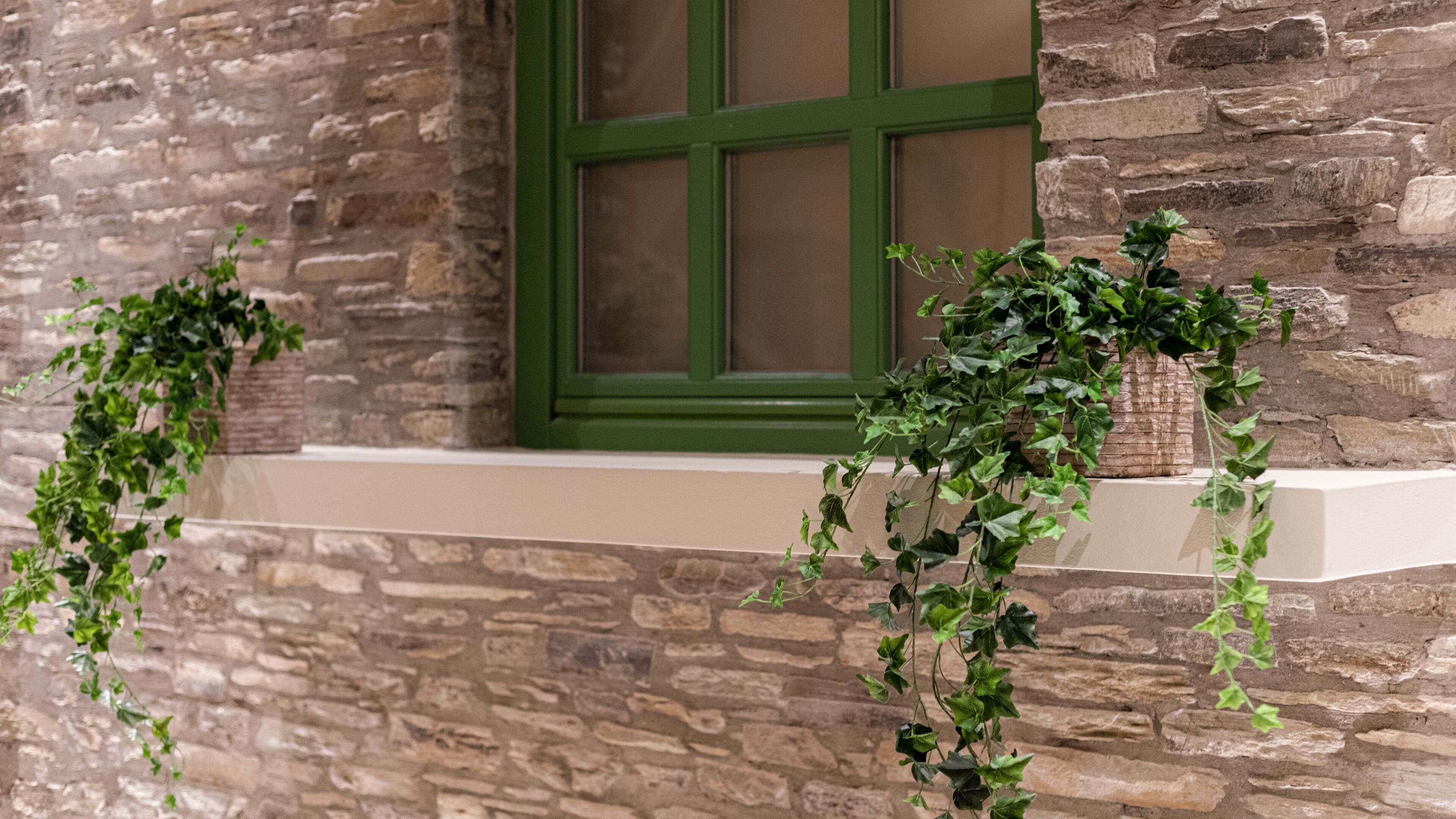A stone building with a green window and two hanging planters with green vines.