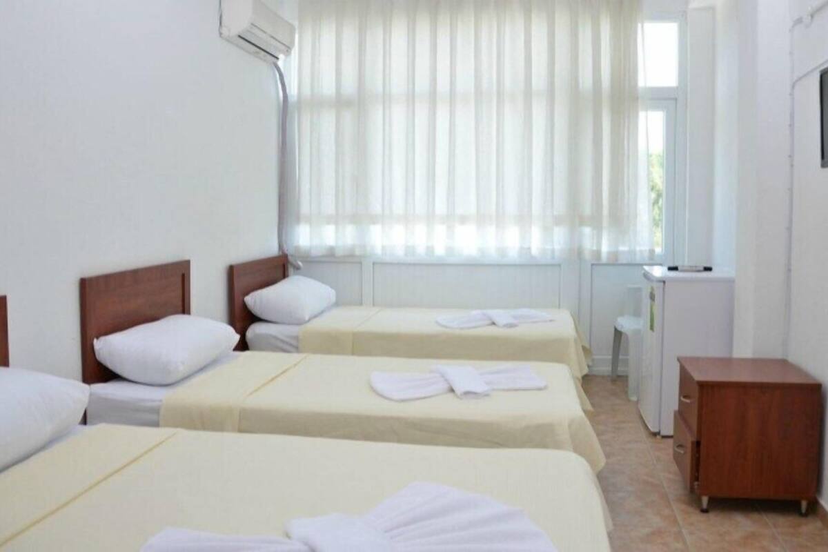 A hotel room with three single beds, a small wooden cabinet, a television, and a window with sheer curtains.