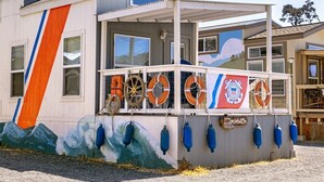 Un edificio con porche cubierto, boyas salvavidas y un mural de olas.