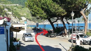 Eine Küstenstraße mit parkenden Autos, einer roten Fahrbahnmarkierung und Blick auf das Meer.