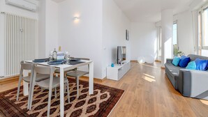 Un soggiorno moderno con zona pranzo, un divano grigio con cuscini blu, una TV a schermo piatto e un tappeto decorato.