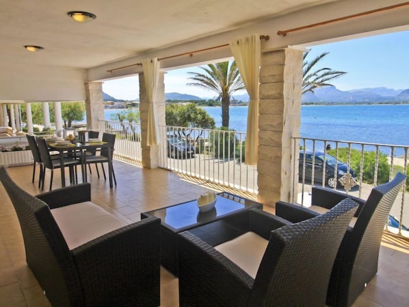A terrace with wicker furniture, a dining table, and a view of the sea and mountains.