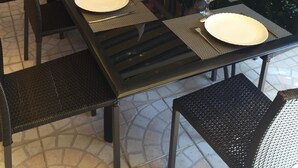 Een terras met een lange tafel voor zes personen, omringd door rieten stoelen.