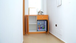 Une petite chambre équipée d’un mini-réfrigérateur intégré contenant des boissons, d’une petite armoire en bois et d’un miroir mural.