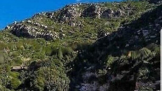 Une plage bordée d’une eau turquoise et limpide, avec une colline rocheuse en arrière-plan.