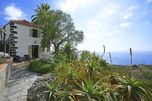 A white building with a stone facade, a stone pathway, and a view of the sea. - Villa El Buen Jesús (Tijarafe)