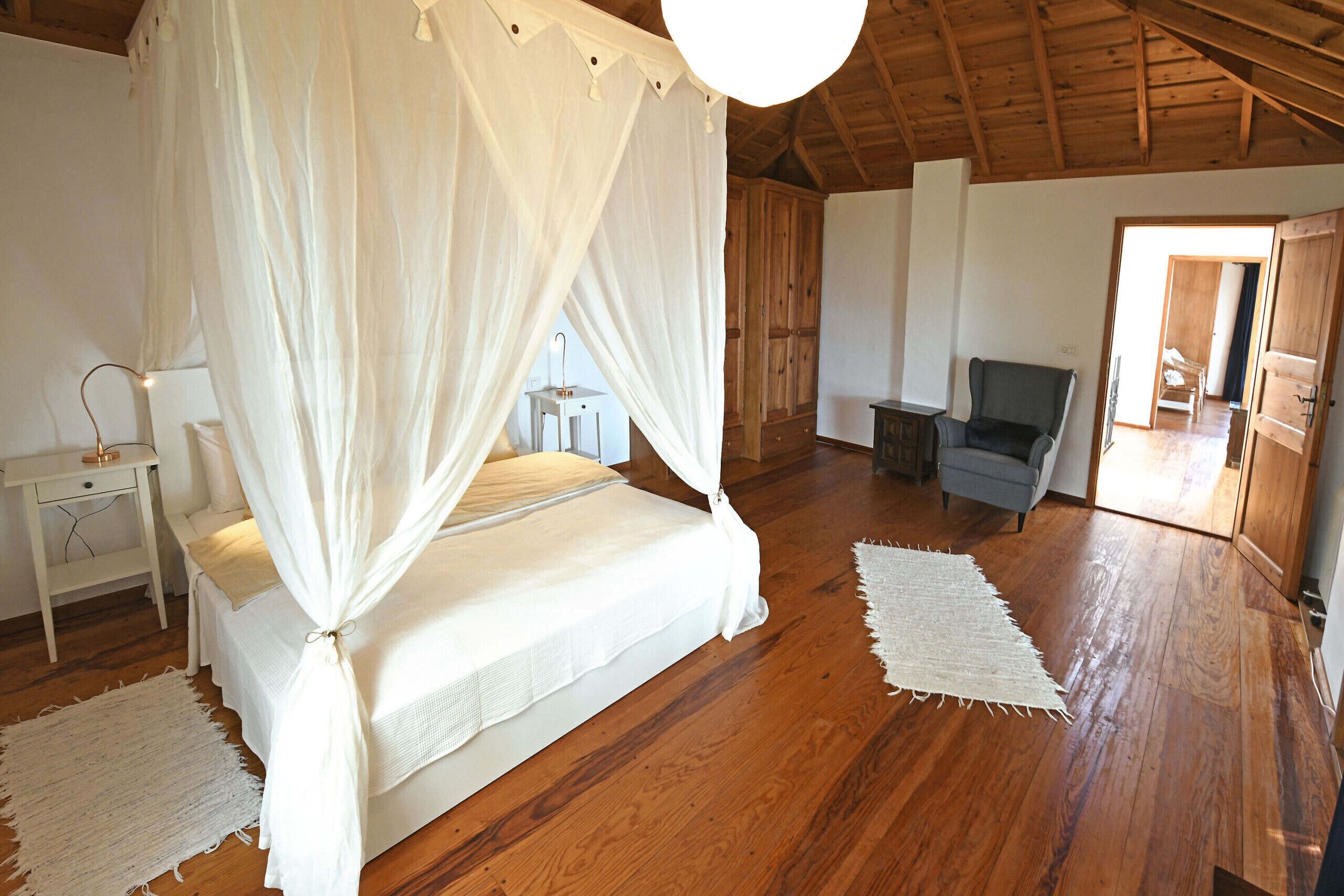 A bedroom with a four-poster bed, wooden flooring, a desk, and a chair.
