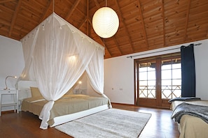 A bedroom with a canopy bed, wooden ceiling, large windows, and a nightstand with a lamp. - Villa El Buen Jesús (Tijarafe)