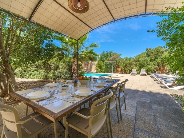 An outdoor dining area with a table set for four, surrounded by chairs, under a canopy.