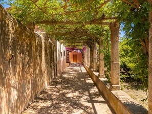 A narrow, stone-walled corridor with a wooden archway at the end, surrounded by greenery and trees.