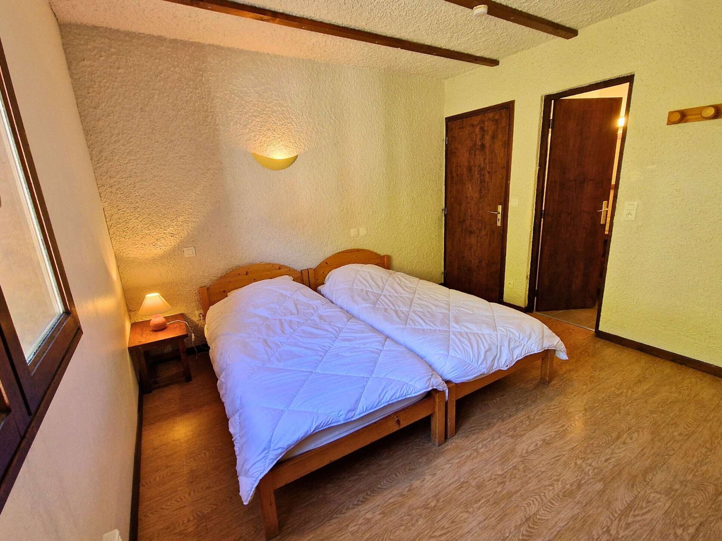 A room with a bed, a nightstand, a wall-mounted light, and two wooden doors.
