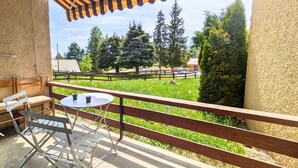 A balcony with a striped awning, a table with chairs, and a view of a green field and trees. - Ground Floor Apartment for 6 - Balcony - Pets Welcome - Saint-Michel-de-Chaillol (Saint-Michel-de-Chaillol)