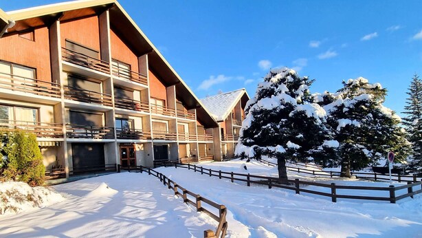 A multi-story building with balconies, a snow-covered courtyard, and a wooden fence. - Ground Floor Apartment for 6 - Balcony - Pets Welcome - Saint-Michel-de-Chaillol (Saint-Michel-de-Chaillol)