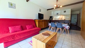 A red sofa, wooden coffee table, dining table with chairs, a TV, and a kitchen area. - Ground Floor Apartment for 6 - Balcony - Pets Welcome - Saint-Michel-de-Chaillol (Saint-Michel-de-Chaillol)