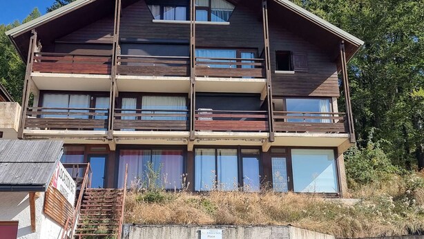 A multi-story wooden building with balconies, large windows, and a staircase leading to the entrance.