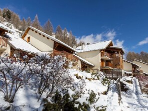 Ein Chalet mit mehreren Balkonen, umgeben von schneebedeckten Bäumen und einem klaren Himmel.