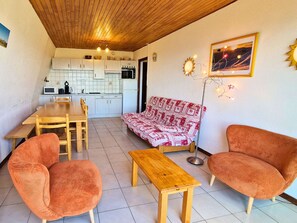 A compact living space with a wooden ceiling, a kitchenette, a dining area, and a sofa.