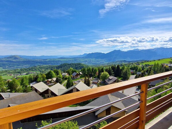 Ein Wohngebiet mit Häusern, einem Holz-Balkon und einer bergigen Landschaft im Hintergrund.