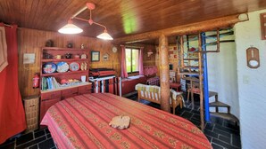 A cozy cabin-style room with a wooden ceiling, a large bed with a red floral bedspread, a wooden bookshelf, and a small desk with a chair.
