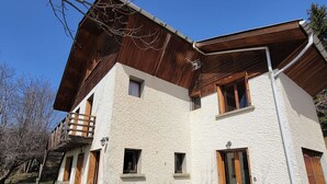 A two-story building with a wooden balcony, a stone foundation, and a white textured exterior.