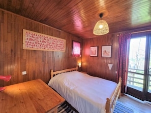 Ein Zimmer mit Holzwandverkleidung, einem Bett, einem Tisch und einer Hängelampe.