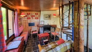 A cozy cabin interior with a wooden ceiling, a fireplace, a television, and a seating area with benches and a table.
