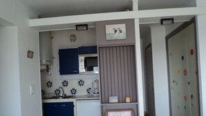 Une cuisine de taille réduite avec des meubles bleus, un four à micro-ondes et un évier. Un élément décoratif orne le mur au-dessus de l’évier, et un tableau encadré est posé sur une étagère.