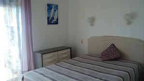 Une chambre à coucher avec un lit, une table de chevet, un tableau et une fenêtre avec des rideaux.