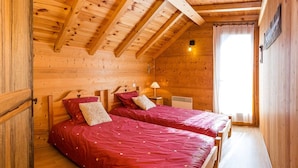 Une chambre dans un chalet en bois, avec deux lits, une table de chevet, une lampe et une fenêtre avec des rideaux.