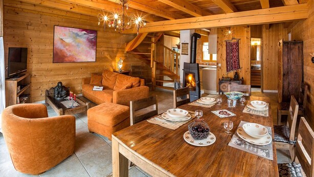 Un intérieur chaleureux, avec des murs en bois, une table à manger dressée pour quatre personnes, un canapé et une cheminée.