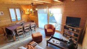 L’intérieur d’un chalet en bois accueillant, avec une table à manger, des chaises, un canapé, un téléviseur et une bibliothèque.