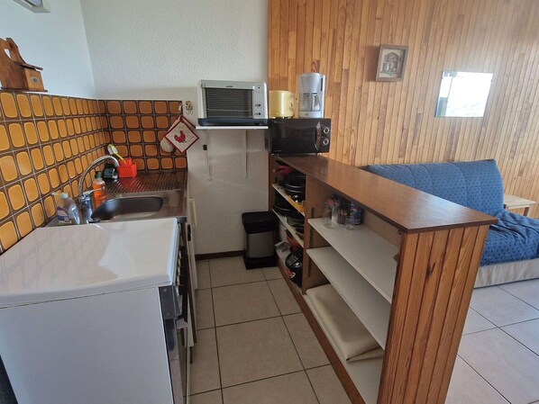A compact kitchen with a sink, a microwave, and a coffee maker on a shelf.