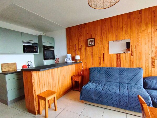 A compact living space with a kitchenette, a wooden wall, a blue sofa, and a small wooden table.