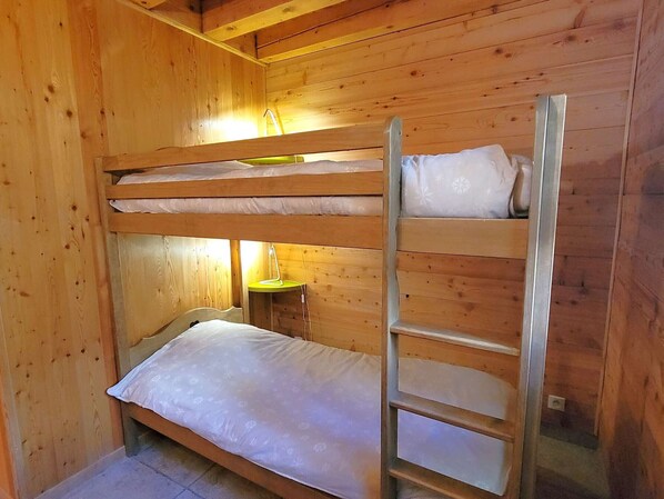 A bunk bed room with wooden walls, a small bedside table with a lamp, and a ladder for access to the upper bunk.