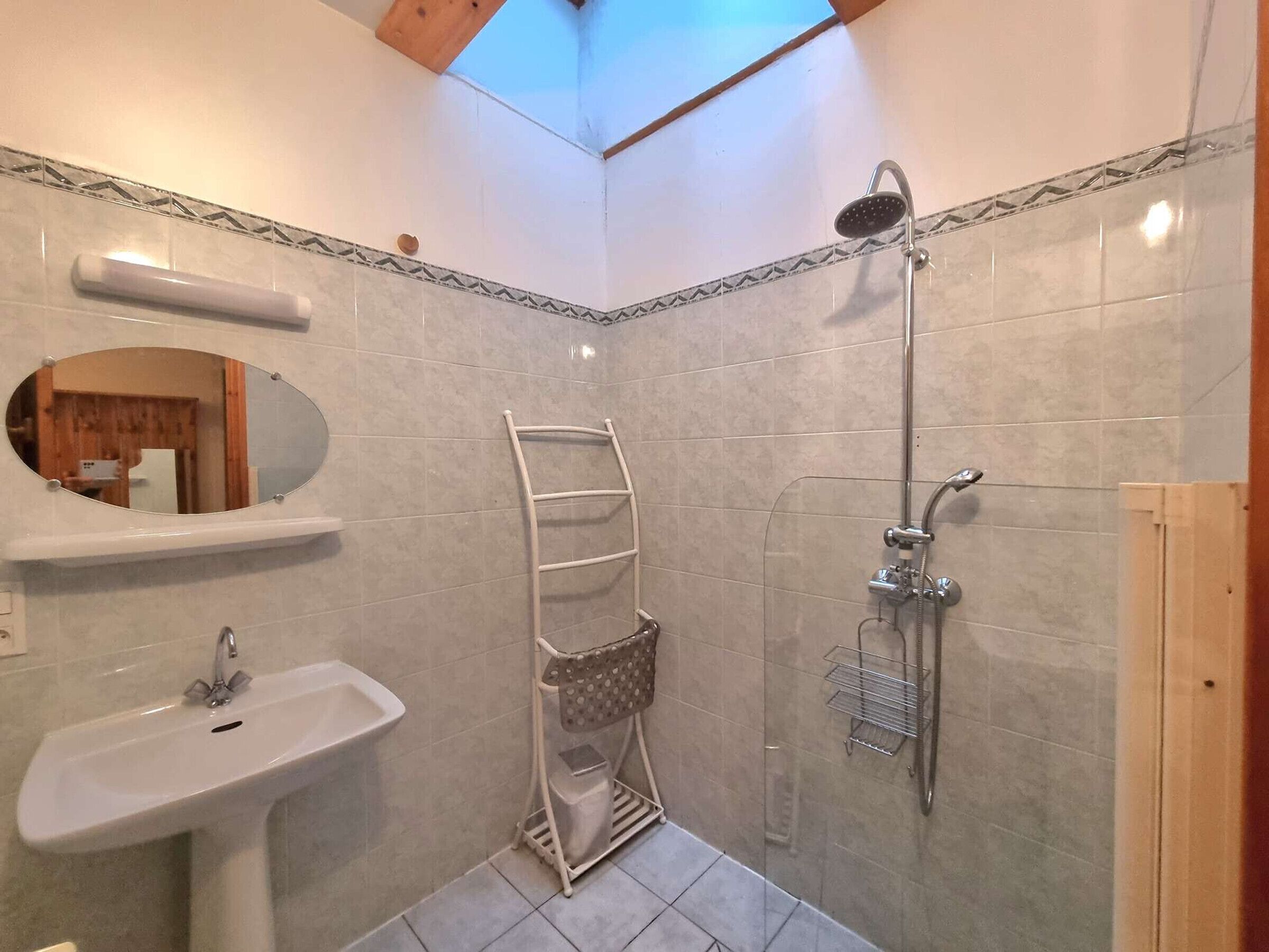 Een badkamer met een wastafel, spiegel, handdoekrek, douche en dakraam.