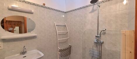 Een badkamer met een wastafel, spiegel, handdoekrek, douche en dakraam.