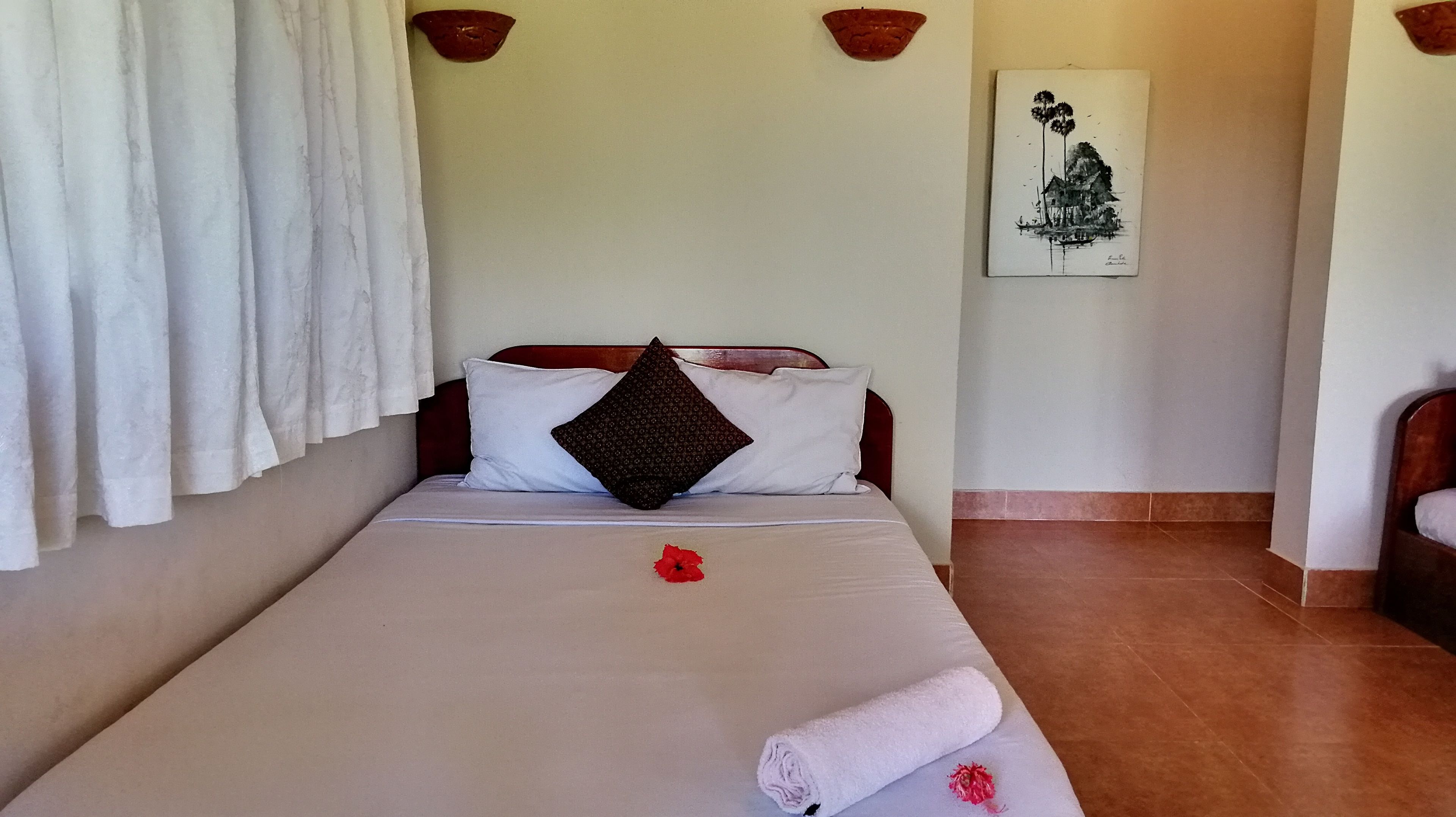 A neatly made bed with white linens, a red flower, and a rolled towel.