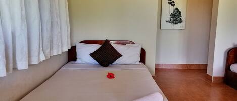 A neatly made bed with white linens, a red flower, and a rolled towel.
