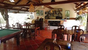 Zona de bar con mobiliario de madera, mesa de billar y menú en una pizarra.