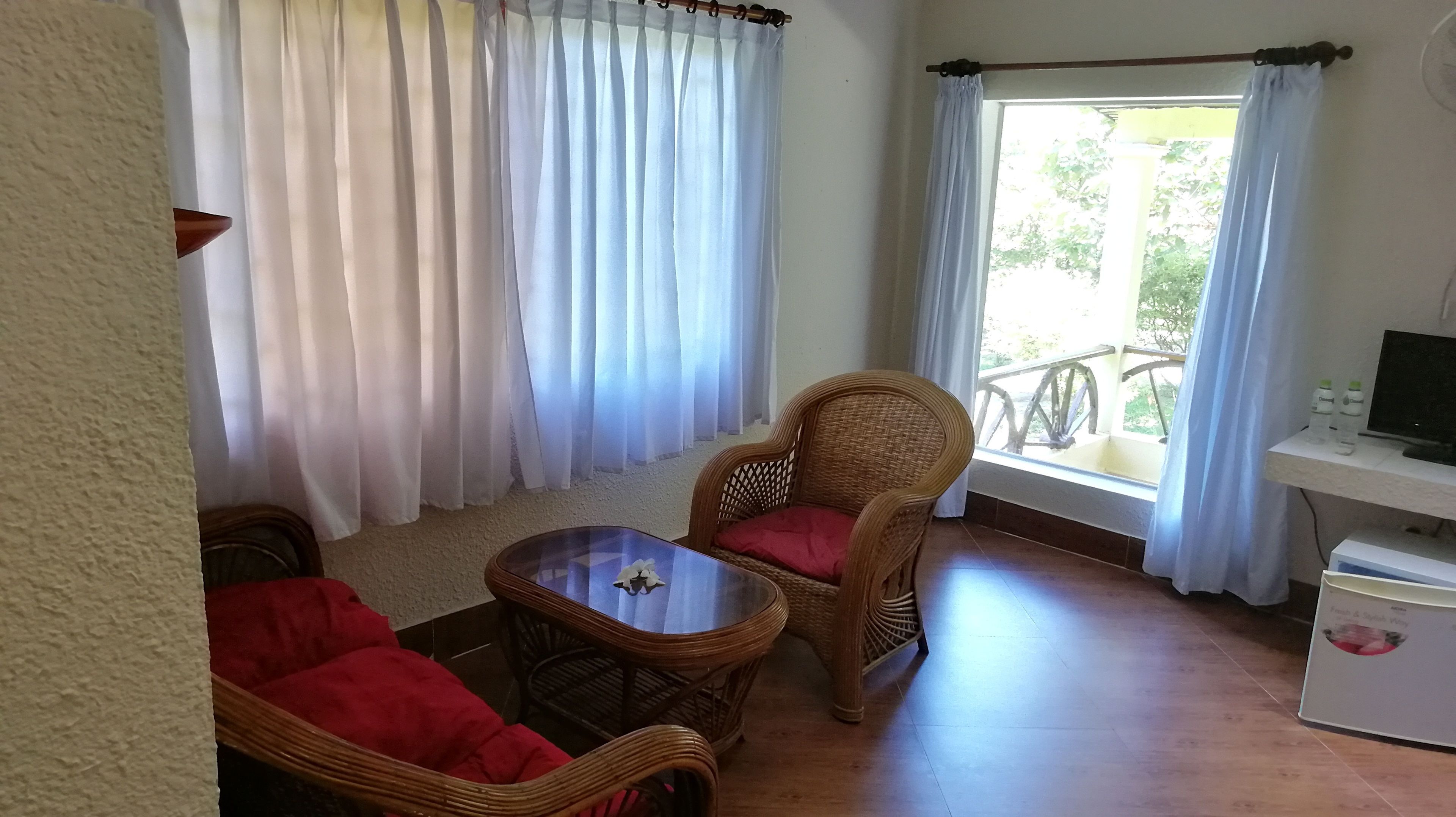 A room with wicker furniture, a small table, a TV, and a window with curtains.