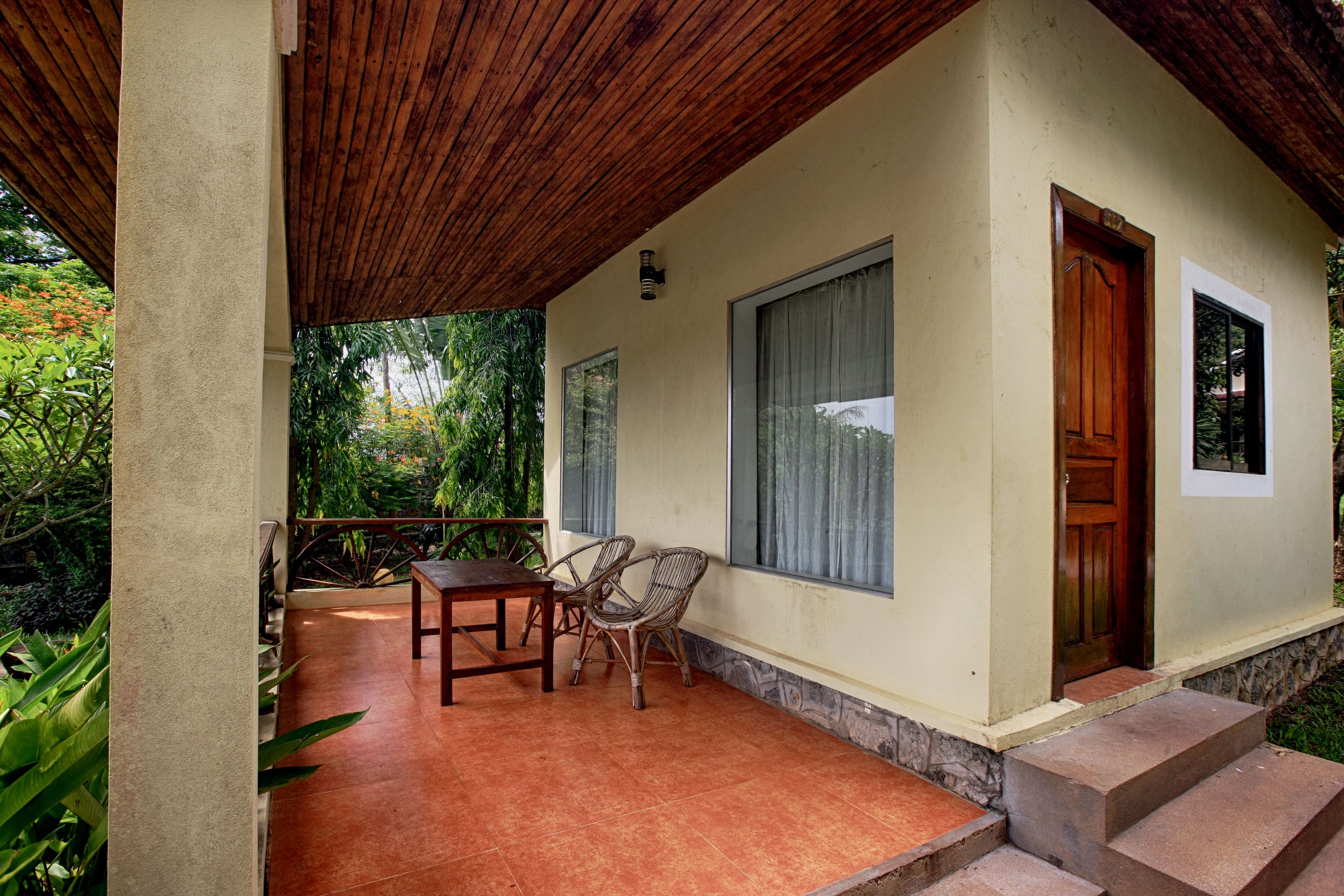 A covered patio area with a wooden table and chairs, a stone wall, and a door.