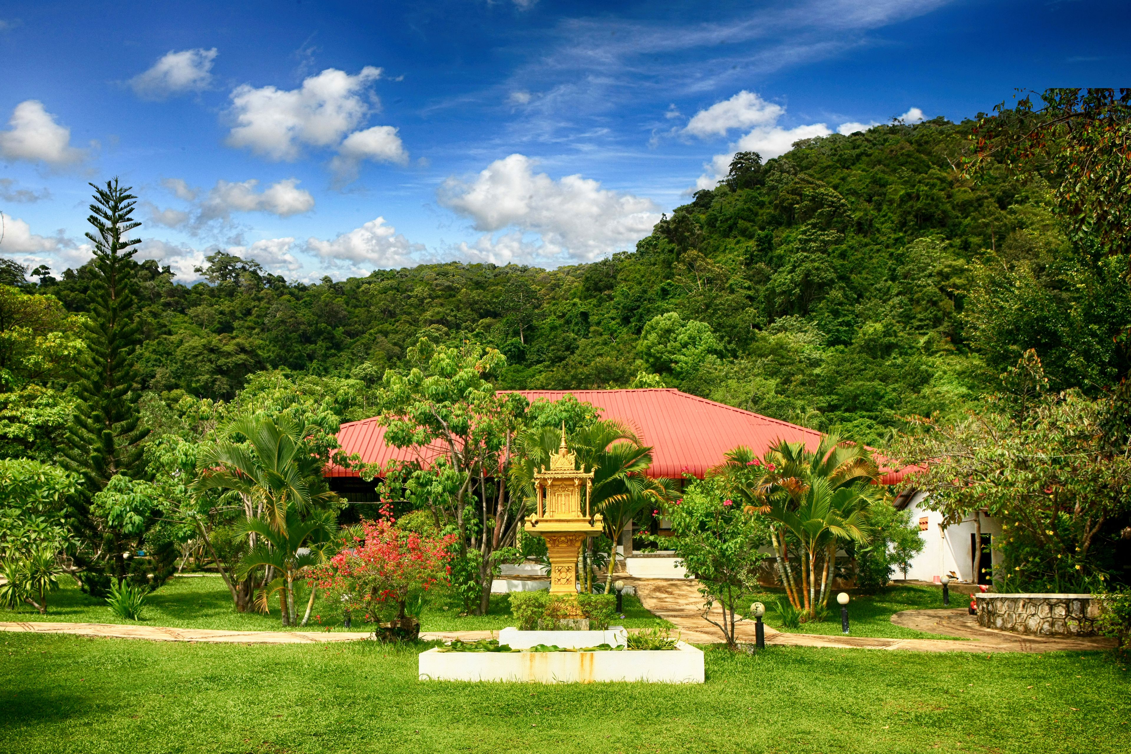 Un jardín exuberante con una fuente, un edificio de techo rojo y una colina al fondo.