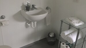 Un bany amb un rentapans, vàter i una prestatgeria de vidre amb tovalloles.